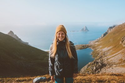 Smilende kvinne står på toppen av et fjell, fjord i bakgrunnen