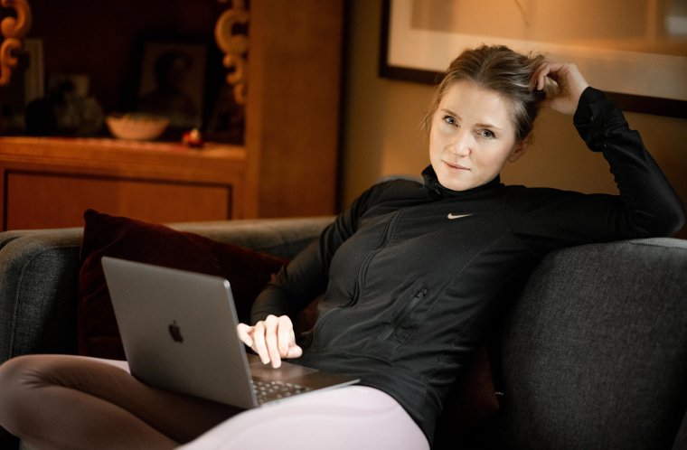 Kvinne i sofa med pc ser i kamera