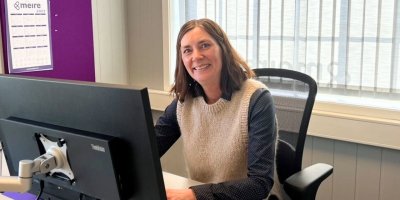 Kvinne smiler mens hun sitter ved en datamaskin på et kontor.