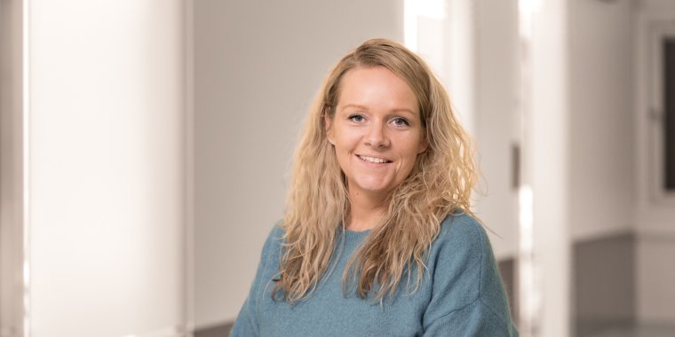 Kvinne med langt blondt hår smiler i et lyst rom.