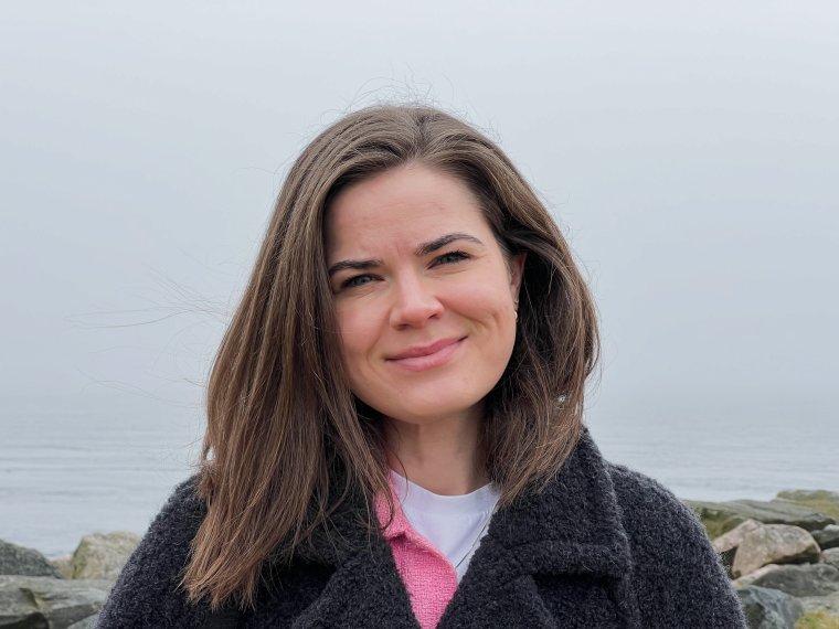 Kvinne smiler i kamera ute ved sjøen