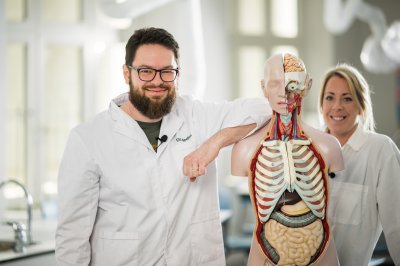 To personer i hvite frakker med en anatomisk modell i et klasserom.