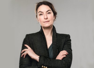 Kvinne i mørk jakke med armene i kors, ser bestemt inn i kameraet.