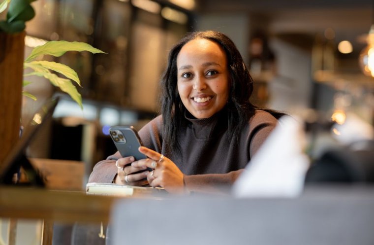 Kvinne smiler mens hun holder en mobiltelefon på en kafé.