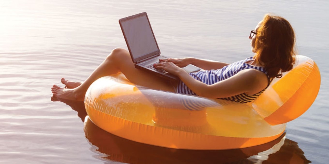 Person jobber på laptop mens de flyter på en badering i vannet.