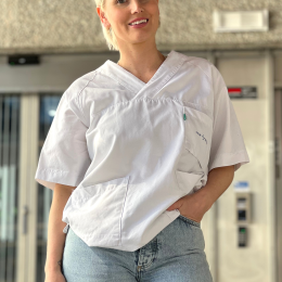 Student i hvit uniform og jeans smiler foran en bygning.
