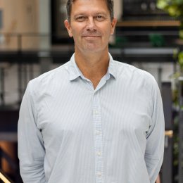 Mann i lyseblå skjorte står foran en moderne kontorbygning.