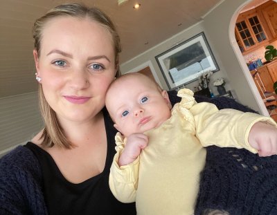 Mor og baby smiler til kameraet i et koselig hjemmemiljø.