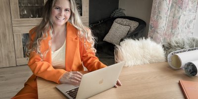 Kvinne i oransje dress jobber på en bærbar datamaskin ved et trebord.