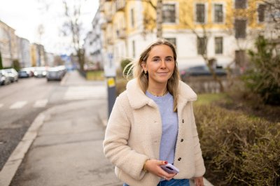 Kvinne i lys jakke går langs en gate med bygninger i bakgrunnen.