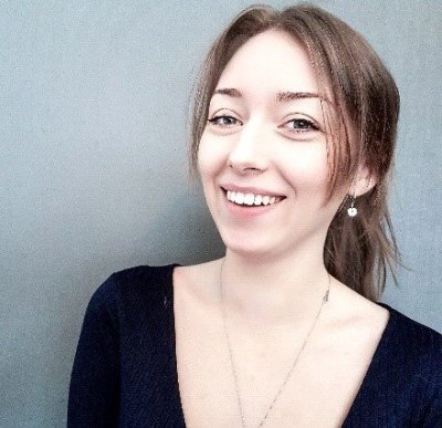 kamilla-ness-mannes2_size-large Smilende kvinne med brunt hår og øredobber foran grå bakgrunn.