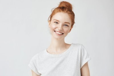 Smilende kvinne med rødlig hår i hvit t-skjorte mot lys bakgrunn.