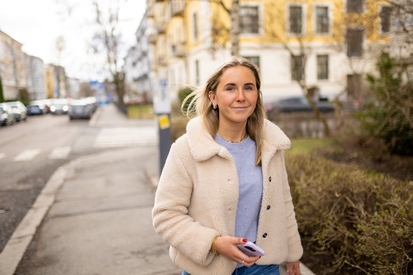Kvinne i lys jakke går langs en gate med bygninger i bakgrunnen.