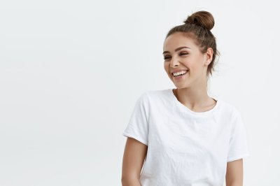 Smilende kvinne i hvit t-skjorte med håret i toppknute mot hvit bakgrunn.