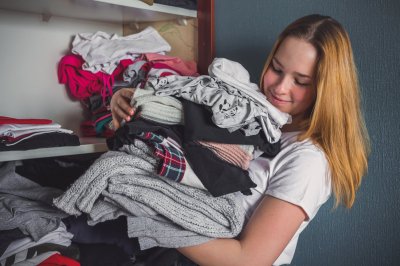 Kvinne smiler mens hun holder en stor bunke med klær foran et skap.