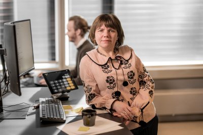 olena Kvinne ved arbeidspult ser inn i kamera