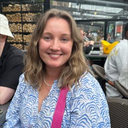 Kvinne smiler mens hun sitter på en utendørs kafé.