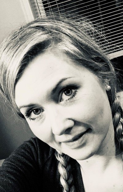 Sort-hvitt portrett av en smilende kvinne med fletter og vindu i bakgrunnen.