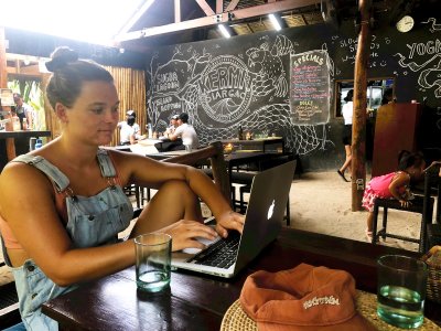 Kvinne studerer på laptop i en kafé med surfetema, med tavlekunst i bakgrunnen.