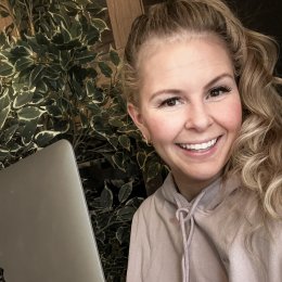 Kvinne smiler foran en bærbar datamaskin med planter i bakgrunnen.
