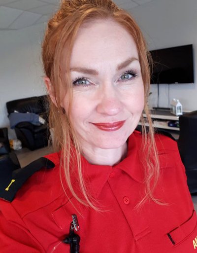 Kvinne i rød uniform smiler foran et kontorområde.