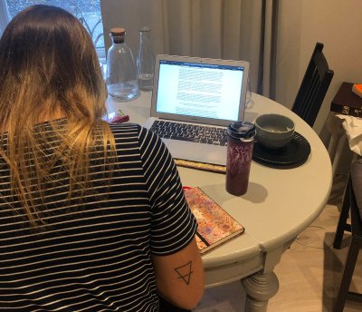 Person studerer ved et rundt bord med laptop, notatbok og drikke.