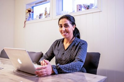 Kvinne smiler mens hun jobber på en bærbar datamaskin ved et bord hjemme.