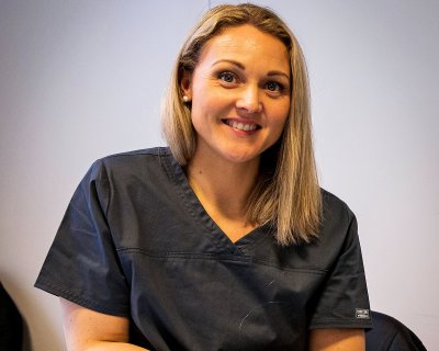 Kvinne i mørk uniform smiler mot kameraet, klar for jobb i helsevesenet.