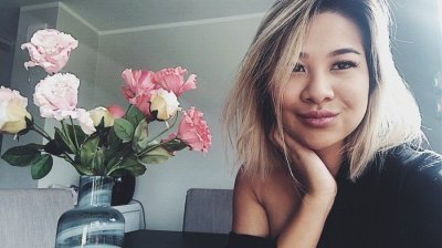 Kvinne smiler ved siden av en vase med blomster i et moderne interiør.