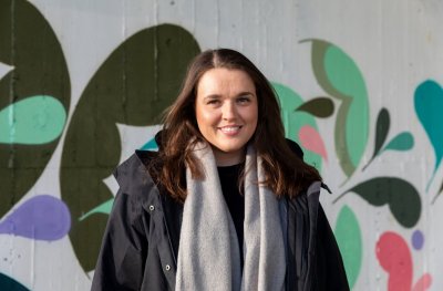 Kvinne smiler foran en fargerik vegg med abstrakt kunst.