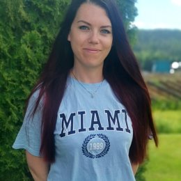 Kvinne med langt hår og "Miami" t-skjorte står ute foran grønn bakgrunn.