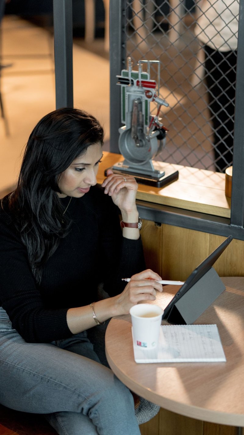 Kvinne studerer på nettbrett med notatblokk og kaffekopp på bordet.