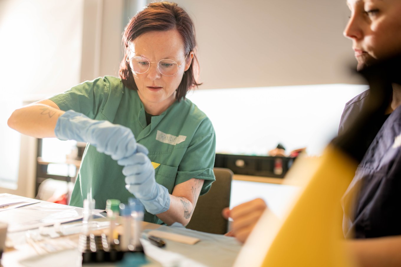 Student i grønn uniform utfører laboratoriearbeid med prøver og utstyr.