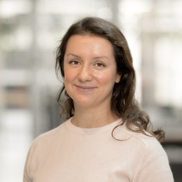 Kvinne smiler foran en uskarp bakgrunn i et moderne kontormiljø.