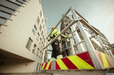 Arbeidere i verneutstyr utfører vedlikehold på en bygning fra en heisplattform.