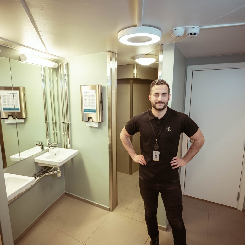Mann i svart t-skjorte står på et moderne bad med vask og speil.