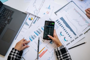 Person analyserer økonomiske grafer og diagrammer med en smarttelefon og bærbar PC.
