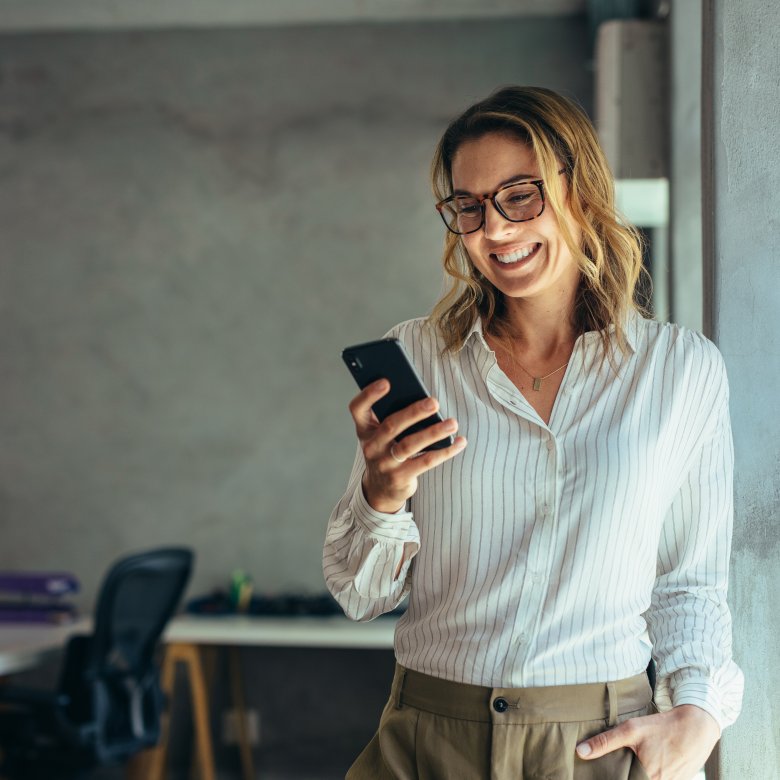 Kvinne smiler mens hun ser på mobilen i et kontor.