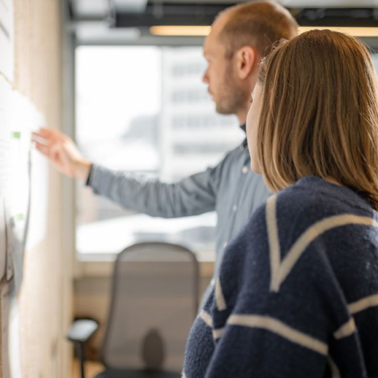 To personer diskuterer et prosjekt ved en tavle på et kontor.