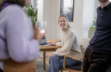 Blid kvinne ved en pc i bakgrunnen