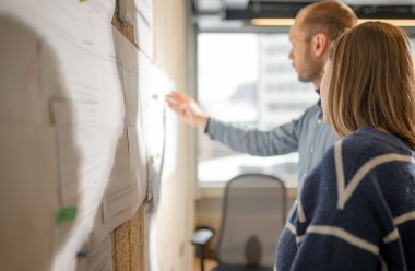 To personer diskuterer et prosjekt ved en tavle på et kontor.