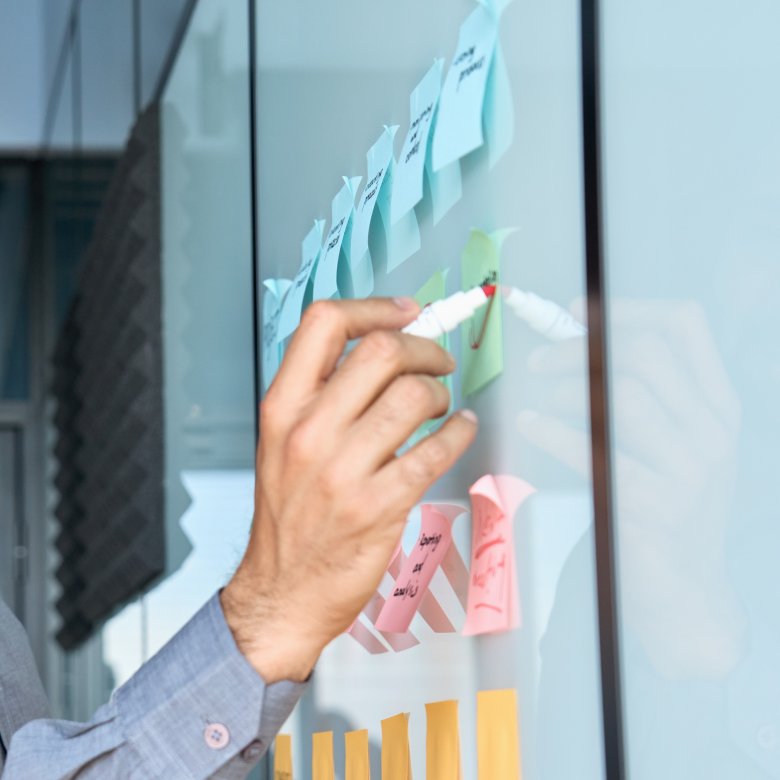 Person skriver på post-it-lapper på en tavle under et prosjektmøte.