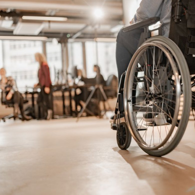 Person i rullestol på kontor, med kolleger i bakgrunnen.
