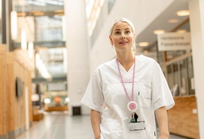 Sykepleier i hvit uniform står i en moderne sykehusgang.