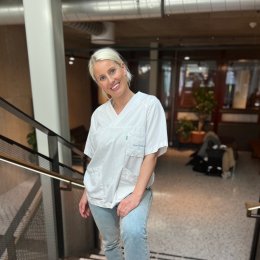 Kvinne i hvit uniform står i en trapp og smiler til kameraet.