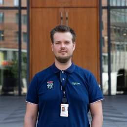 Mann i blå uniform står foran en bygning med glassdører.