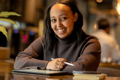 Dame som sitter foran en Ipad og smiler og ser inn i kamera