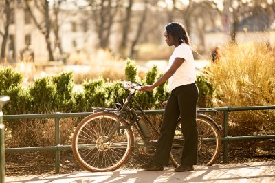 Person i hvit t-skjorte går med sykkel i solfylt park.