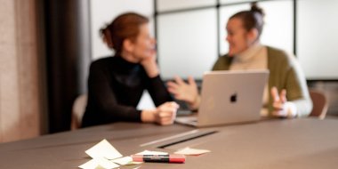 To personer diskuterer ved et bord med bærbar PC og notater.