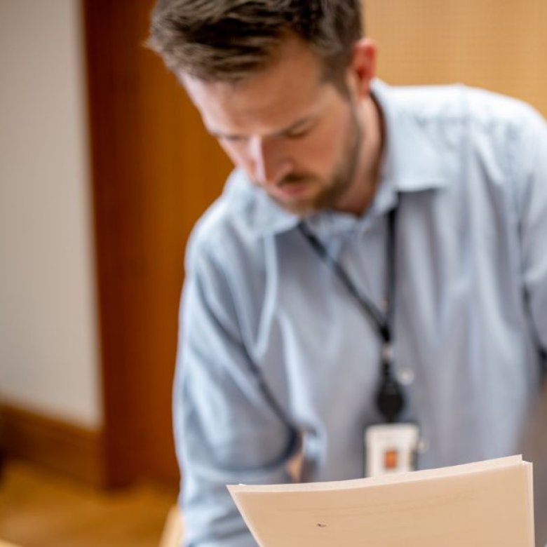 En mann i skjorte leser dokumenter på et kontor.